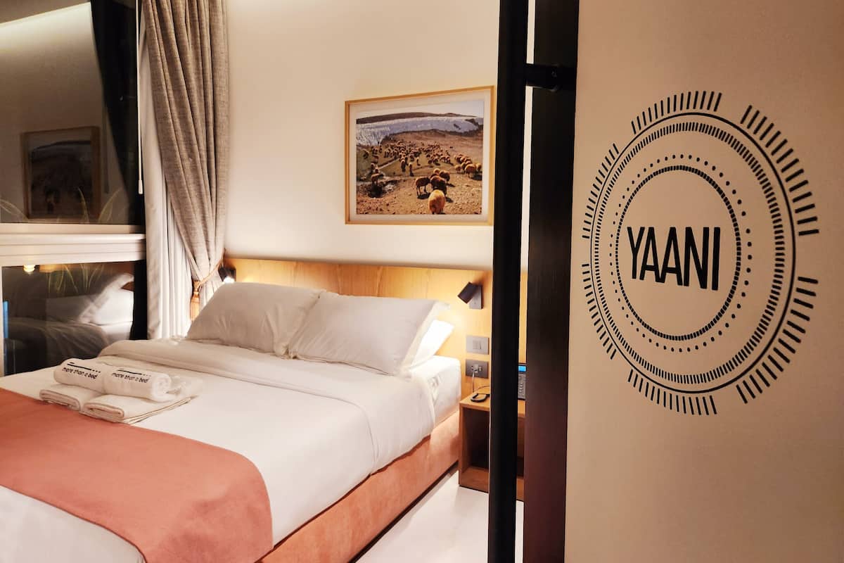 Una habitación de hotel con cama, mesita de noche, un cuadro en la pared y un logotipo en la pared.