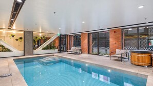 An indoor swimming pool with a tiled floor, a wooden hot tub, and a staircase leading to an upper level. - Hyde Lane 1BR | Walk to Cafes + Pool + Gym (Wellington)