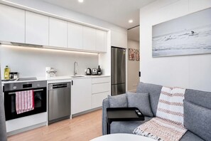 A modern kitchen with white cabinets, stainless steel appliances, and a grey sofa with a patterned throw.