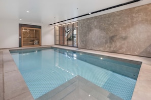 Une piscine intérieure avec un sol carrelé, une porte en bois et une grande fenêtre en verre.