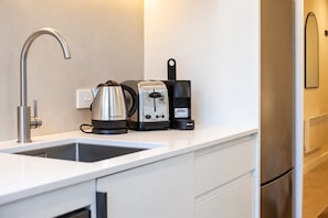 Eine moderne Küche mit Spüle aus Edelstahl, Wasserkocher, Toaster und Kaffeemaschine auf einer weißen Arbeitsplatte.