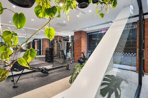Ein modernes Fitnessstudio mit Trainingsgeräten, einem großen Spiegel und einer Glaswand mit Blick auf eine Straße.