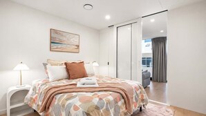 A modern bedroom with a bed, bedside tables, a painting, and a view of a balcony. - Hyde Lane 1BR | Walk to Cafes + Pool + Gym (Wellington)