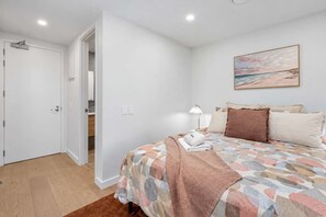 Ein Schlafzimmer mit einem Bett, Kissen, einer Decke, einer Lampe und einem Bild an der Wand.
