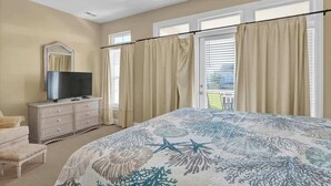 Une chambre à coucher avec un lit, un téléviseur posé sur une commode et un balcon avec des rideaux.