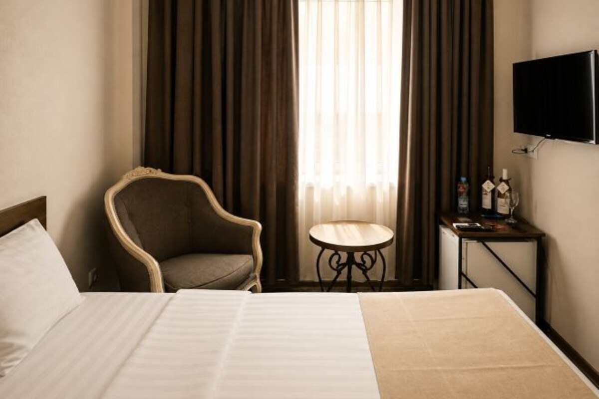 Une chambre d’hôtel avec un lit, une chaise, une petite table ronde et un téléviseur fixé au mur.