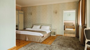 Ein Schlafzimmer mit einem großen Bett, einem Nachttisch, einem Kleiderschrank und Blick auf ein Wohnzimmer durch eine offene Tür.