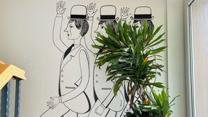 Ein Wandbild mit drei stilisierten Figuren auf einer Treppe, einem Blumentopf und einem Holengeländer.