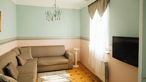 Ein Wohnzimmer mit einem beige-farbenen Sofa, einer Kristallleuchtre, einem Fernseher und einer Heizung.