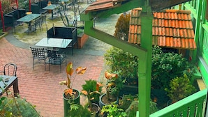 Eine Außenpatio-Terrasse mit Tischen und Stühlen, umgeben von Grünpflanzen und Blick auf Gebäude im Hintergrund.