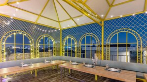 Un restaurant au design moderne, avec des tables et des bancs en bois, un plafond orné de motifs et de grandes fenêtres en arc de cercle.