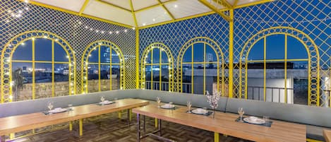 Un restaurant au design moderne, avec des tables et des bancs en bois, un plafond orné de motifs et de grandes fenêtres en arc de cercle.