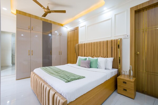 A bedroom with a large bed, wooden wardrobe, and a bedside table. - Alaya Stays Miyabi Executive Suite, Elegant 1-BHK Suite With Common Pool, Gym & Restaurant (Gurugram)