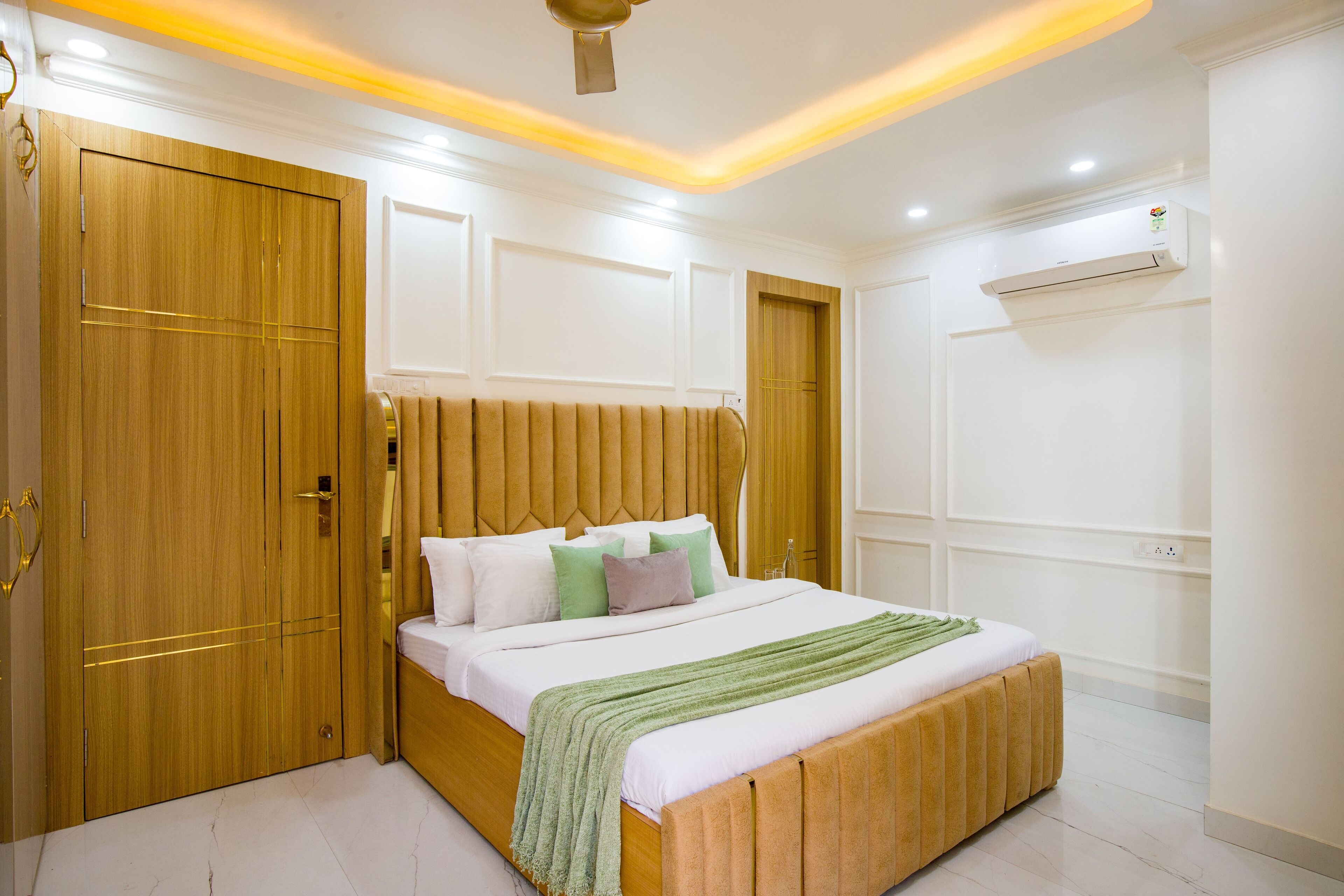 Une chambre avec une armoire en bois, un lit recouvert d’une couverture verte et un climatiseur fixé au mur.