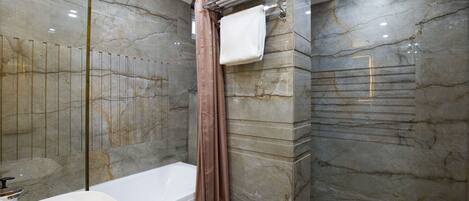 Un baño moderno con bañera, cabina de ducha de vidrio y paredes de mármol.