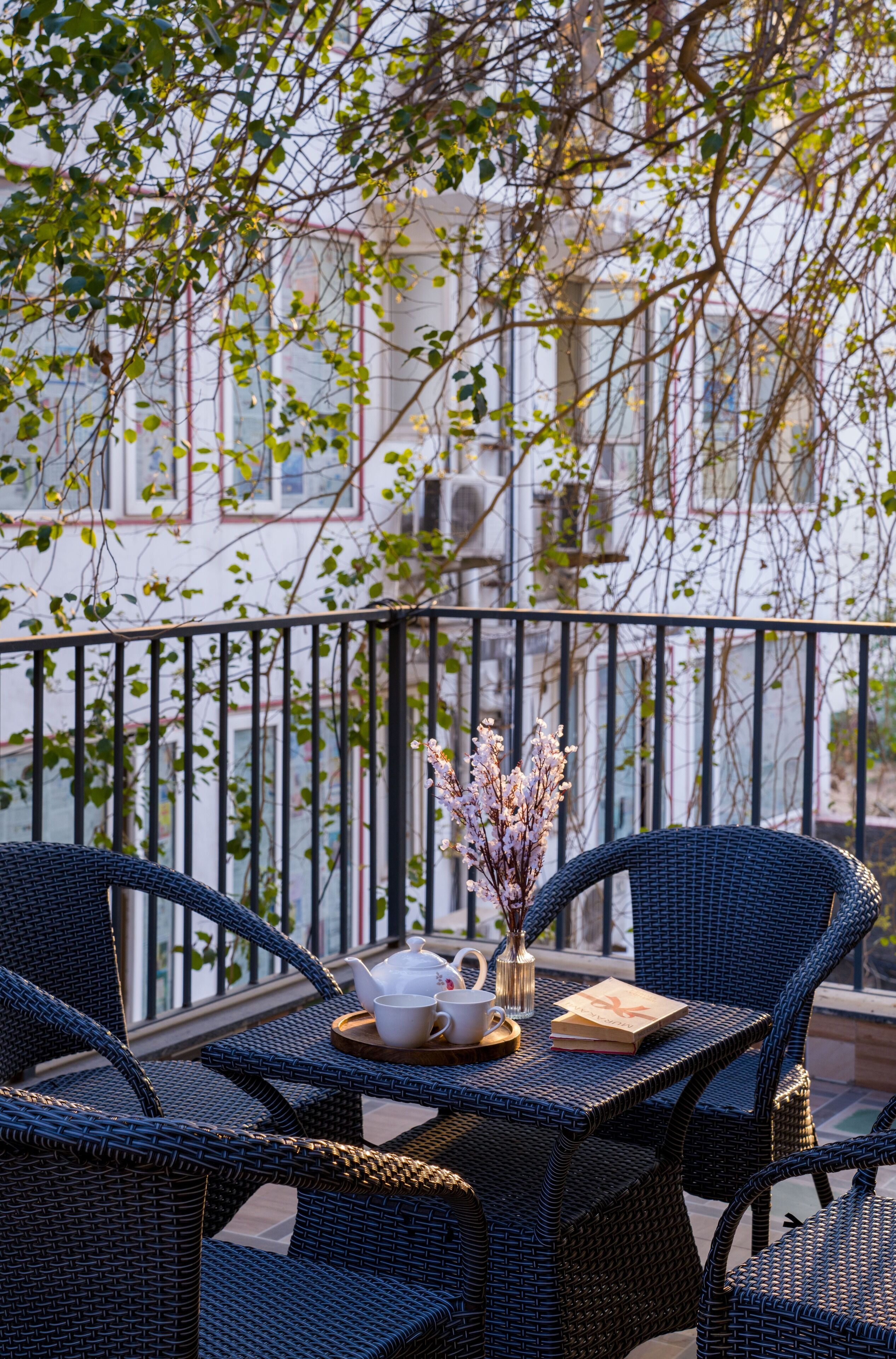 A balcony with wicker furniture, a teapot, a cup, and a vase with flowers.
