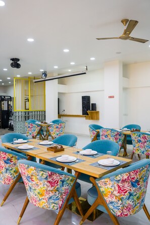A dining area with a long wooden table, blue floral chairs, and a ceiling fan. - Alaya Stays Miyabi Executive Suite, Elegant 1-BHK Suite With Common Pool, Gym & Restaurant (Gurugram)