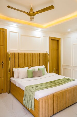 A bedroom with a bed, wooden headboard, and a ceiling fan. - Alaya Stays Miyabi Executive Suite, Elegant 1-BHK Suite With Common Pool, Gym & Restaurant (Gurugram)