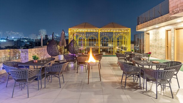 Une terrasse extérieure aménagée avec des meubles en osier, un foyer central et un belvédère illuminé de lumières jaunes.