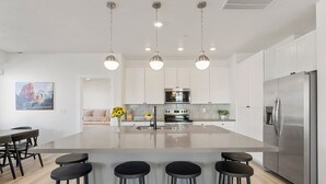 A modern kitchen with a large island, stainless steel appliances, and bar stools. - Sand Cove Retreat 5 Bedroom Townhouse (Hurricane)