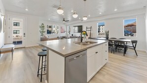 A spacious kitchen with a large island, modern pendant lights, and a dishwasher. - Sand Cove Retreat 5 Bedroom Townhouse (Hurricane)