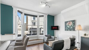 A modern living room with a sofa, armchairs, a TV, and a large window offering a city view.