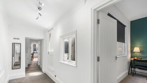 A hallway with white walls, a door with a black blind, and a lamp on a side table.