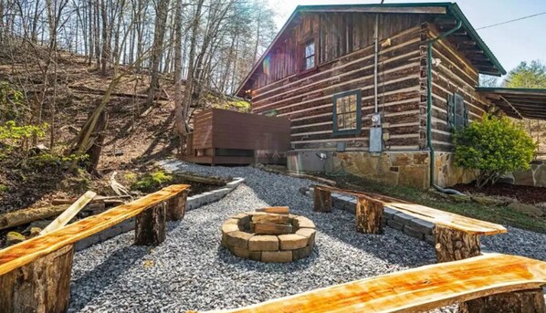 Situated in a wooded area, this cabin offers a natural and secluded environment with a fire pit and benches for guests.
