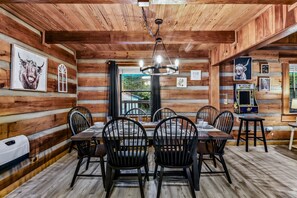 A log cabin interior with a dining table, chairs, a chandelier, and framed artwork on the walls.