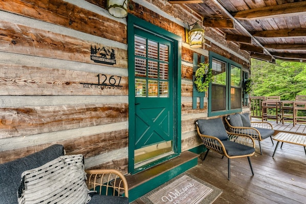 A log cabin with a green door, wicker chairs, and a wooden deck.