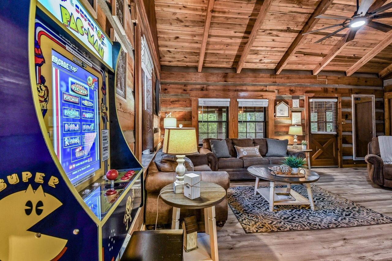 L’intérieur d’une cabane en rondins, avec une borne d’arcade Pac-Man, un salon doté d’un canapé et d’une table basse, et un ventilateur de plafond.