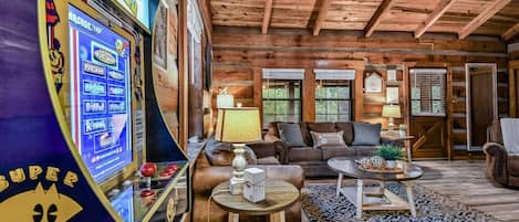 L’intérieur d’une cabane en rondins, avec une borne d’arcade Pac-Man, un salon doté d’un canapé et d’une table basse, et un ventilateur de plafond.