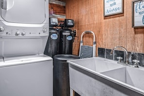 Cocina compacta con lavadora, dos botellas de gas, un cubo de basura y un lavamanos con grifo.