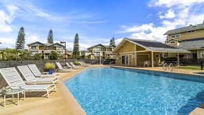 A swimming pool with lounge chairs and a covered area, surrounded by multi-story buildings with balconies. - Big Island Waikoloa Hills 606 2 Bedroom Condo (Waikoloa)