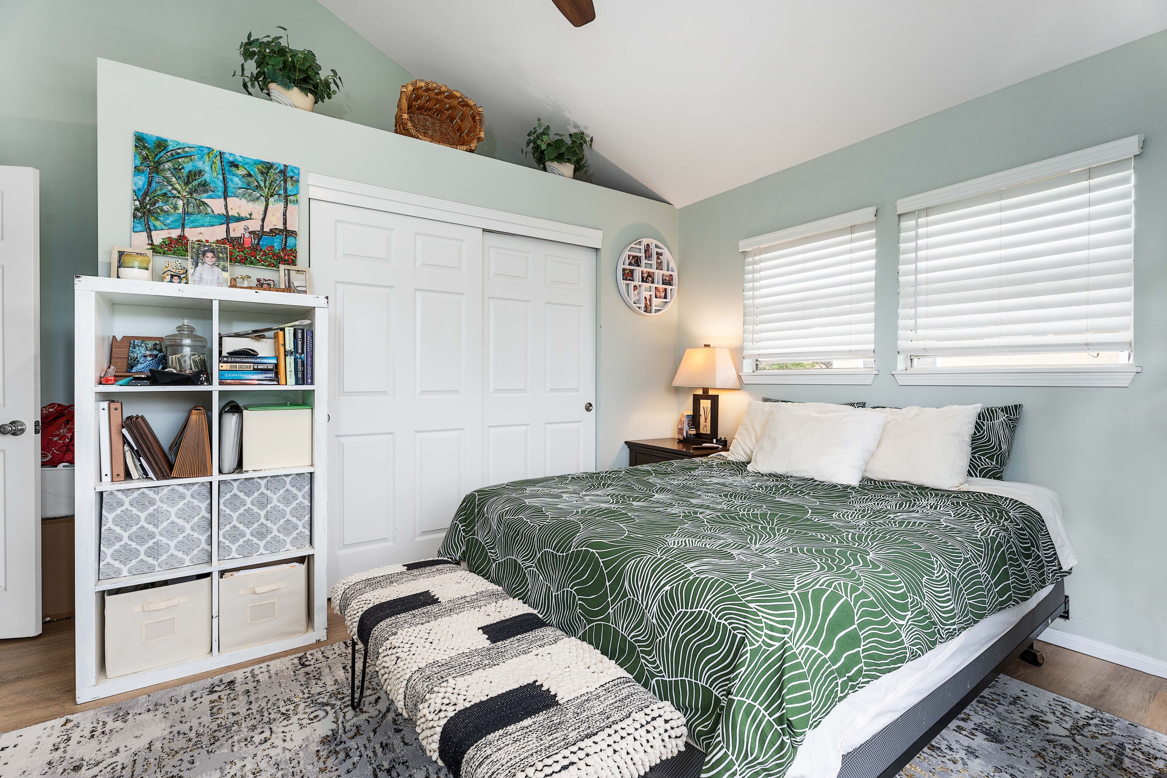 A bedroom with a bed, a white wardrobe, a bookshelf, a round photo wall, and a window with blinds.