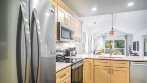 A modern kitchen with stainless steel appliances, wooden cabinets, and a large window providing natural light.