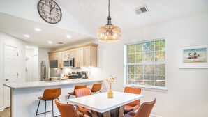 A modern kitchen with white cabinets, a central island, and a dining area with orange chairs.