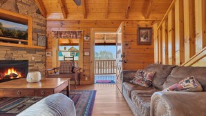 Interior acogedor de una cabaña de troncos con chimenea, muebles de madera y vistas al exterior.