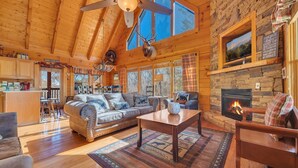 Una cabaña espaciosa con una amplia sala de estar que incluye chimenea, un conjunto de sofás, una mesa de comedor y una cocina.