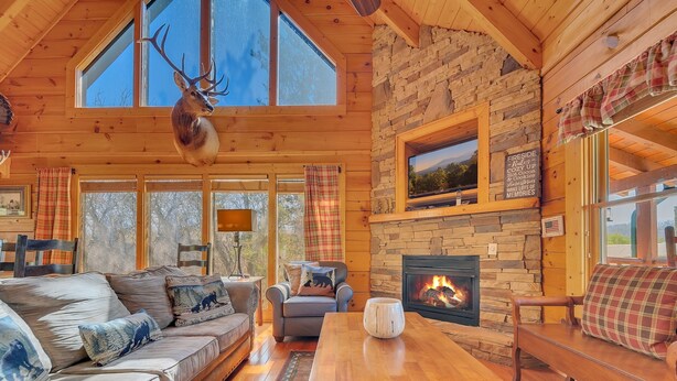 Un interior de cabaña acogedor con chimenea de piedra, mobiliario de madera y ventanas amplias.
