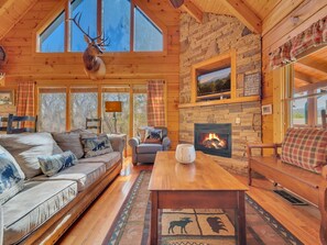 A cozy cabin interior with a stone fireplace, wooden furniture, and large windows. - Ern821 - Tranquil Times 5 Bedroom Cabin (Sevierville)