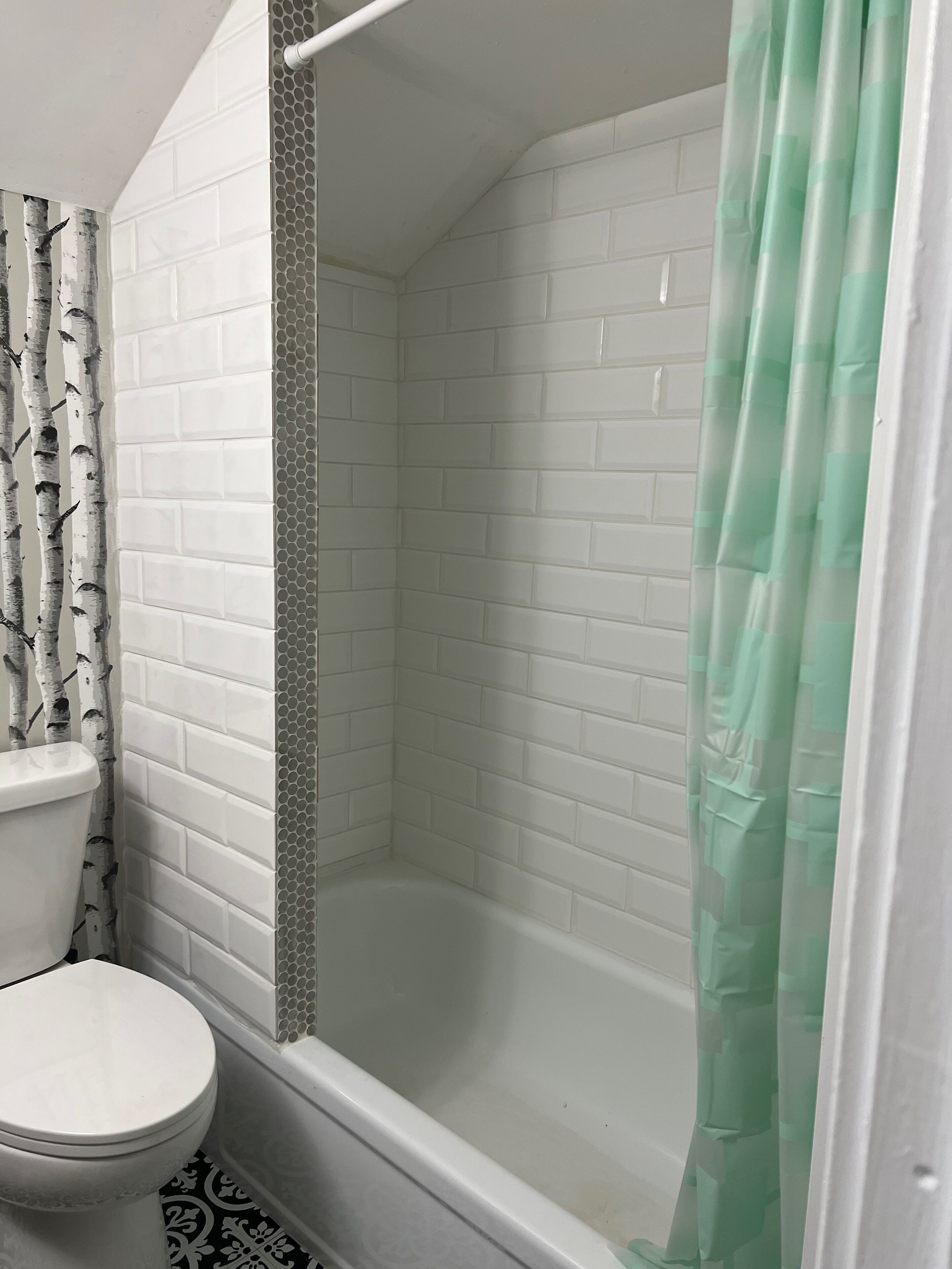 Een badkamer met een wit toilet, een douche met een groen gordijn en een betegelde muur.