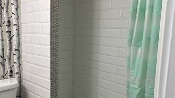 Een badkamer met een wit toilet, een douche met een groen gordijn en een betegelde muur.