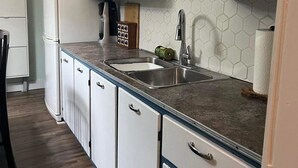 A kitchen with white cabinets, a dark blue upper cabinet, a stainless steel sink, and a hexagonal tile backsplash.