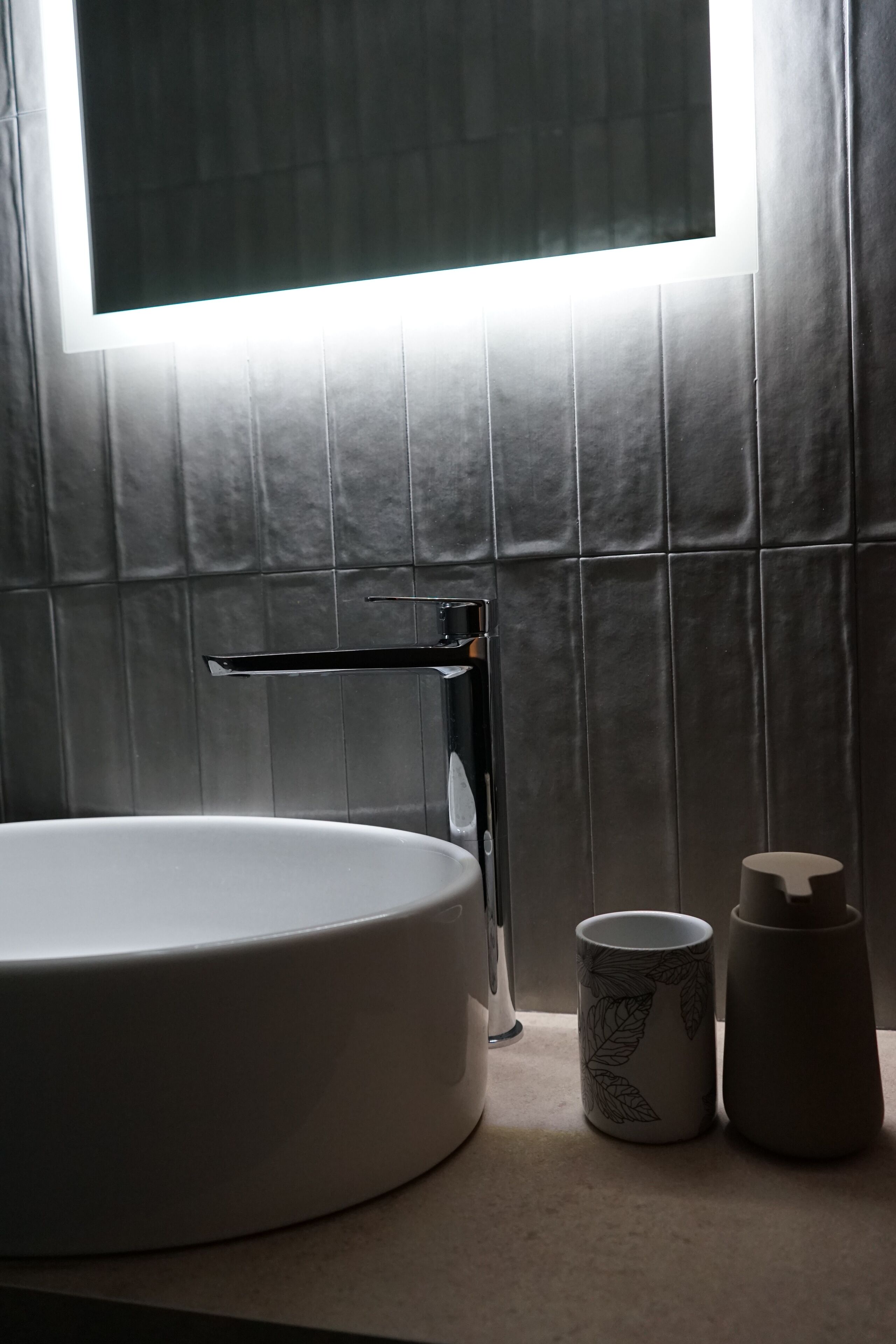 A bathroom with a round sink, a faucet, a mirror, and a window with light streaming through.