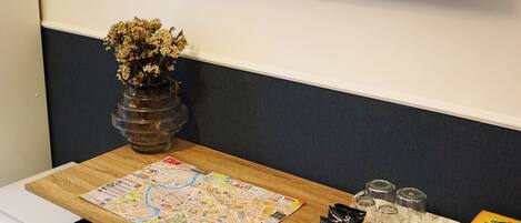 A room with a wooden table, a television displaying 'NETFLIX', a vase with dried flowers, and a small refrigerator.