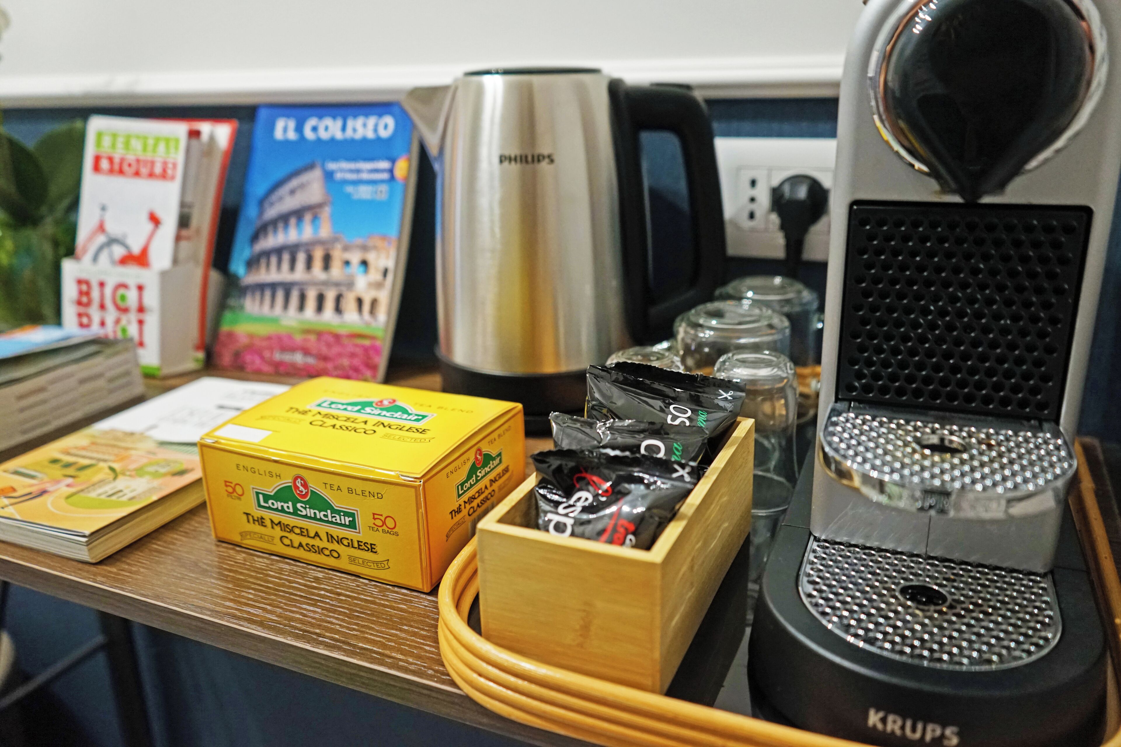 A kitchen counter with a coffee maker, a kettle, a box of tea bags, and a stack of books.