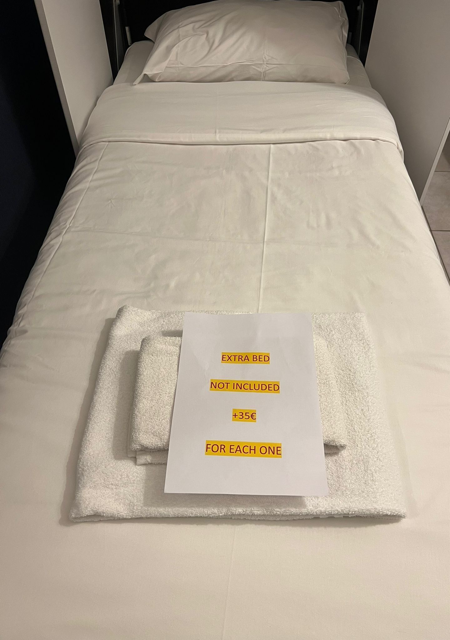 A neatly made bed with a sign indicating an extra bed is not included and a charge of +35€ for each one.