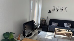 A modern living room with a flat-screen TV, a dark sofa, a wooden coffee table, and a potted plant. - Cosy T2 apartment in Gujan-Mestras 46m2 / Bassin d'Arcachon (Gujan-Mestras)