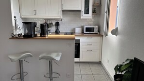 Ett modernt kök med vita skåp, en mikrovågsugn, en kaffebryggare och två barstolar.